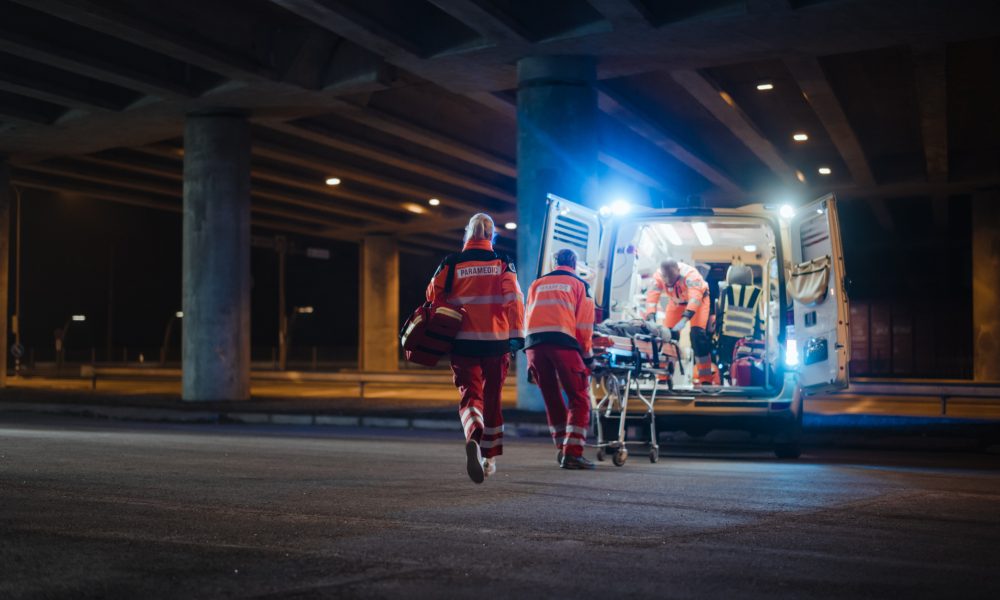 Team of EMS Paramedics React Quick to Provide Medical Help to Injured Patient and Get Him in Ambulance on a Stretcher. Emergency Care Assistants Arrived on the Scene of a Traffic Accident on a Street.